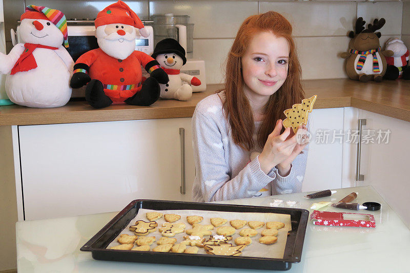 14 / 15岁的红发少女穿着白色衣服，现代厨房里展示着她用糖霜装饰的圣诞饼干